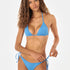 Woman wearing a blue bikini on a white background, tying the side strings