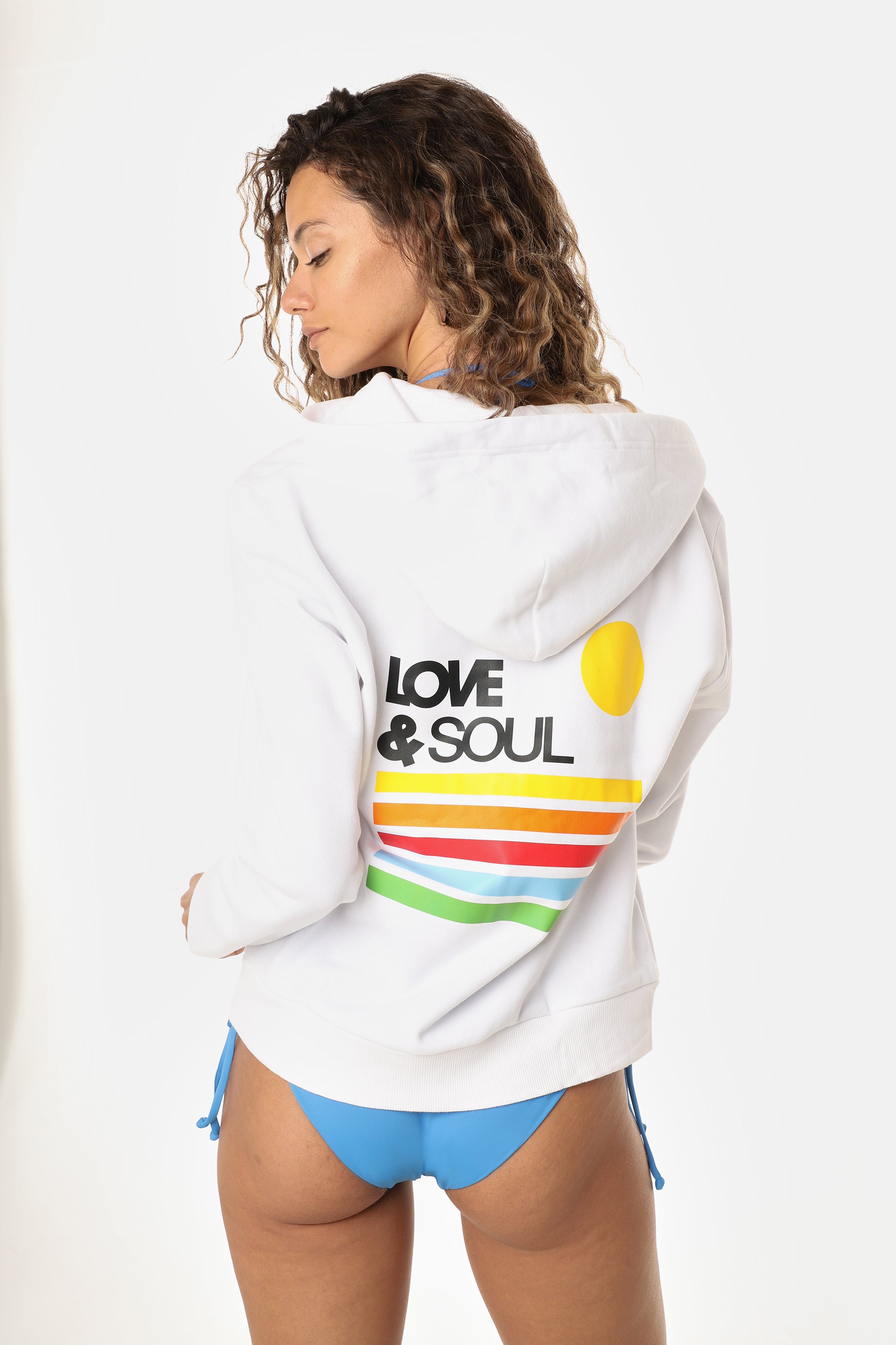 Woman wearing a white hoodie with 'Love & Soul' text and colorful stripes, standing against a white background.